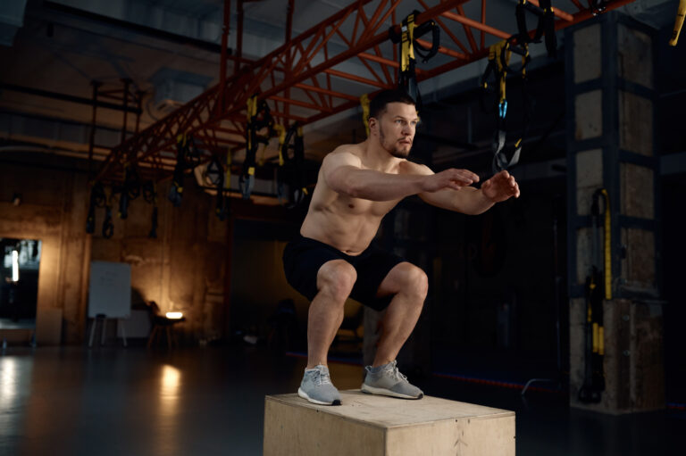 Athletic man doing step-up exercise on wooden box while training in sports club